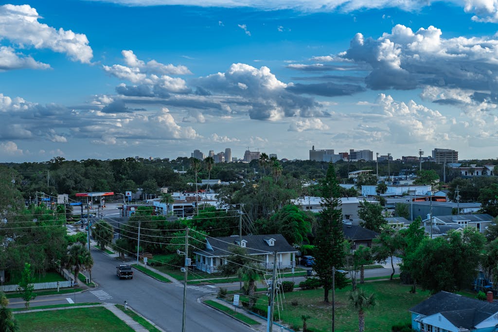Aerial cityscape showcasing residential neighborhood with lush greenery and a vibrant blue sky.